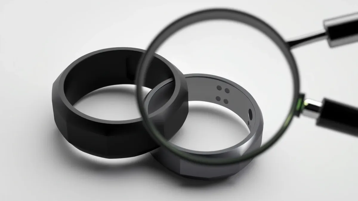 Illustration: A sleek black smart ring rests on a white surface next to a similar silver ring.